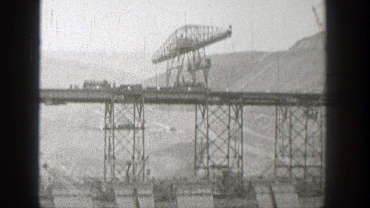 Gantry crane over a steel bridge framework with hills in the background.