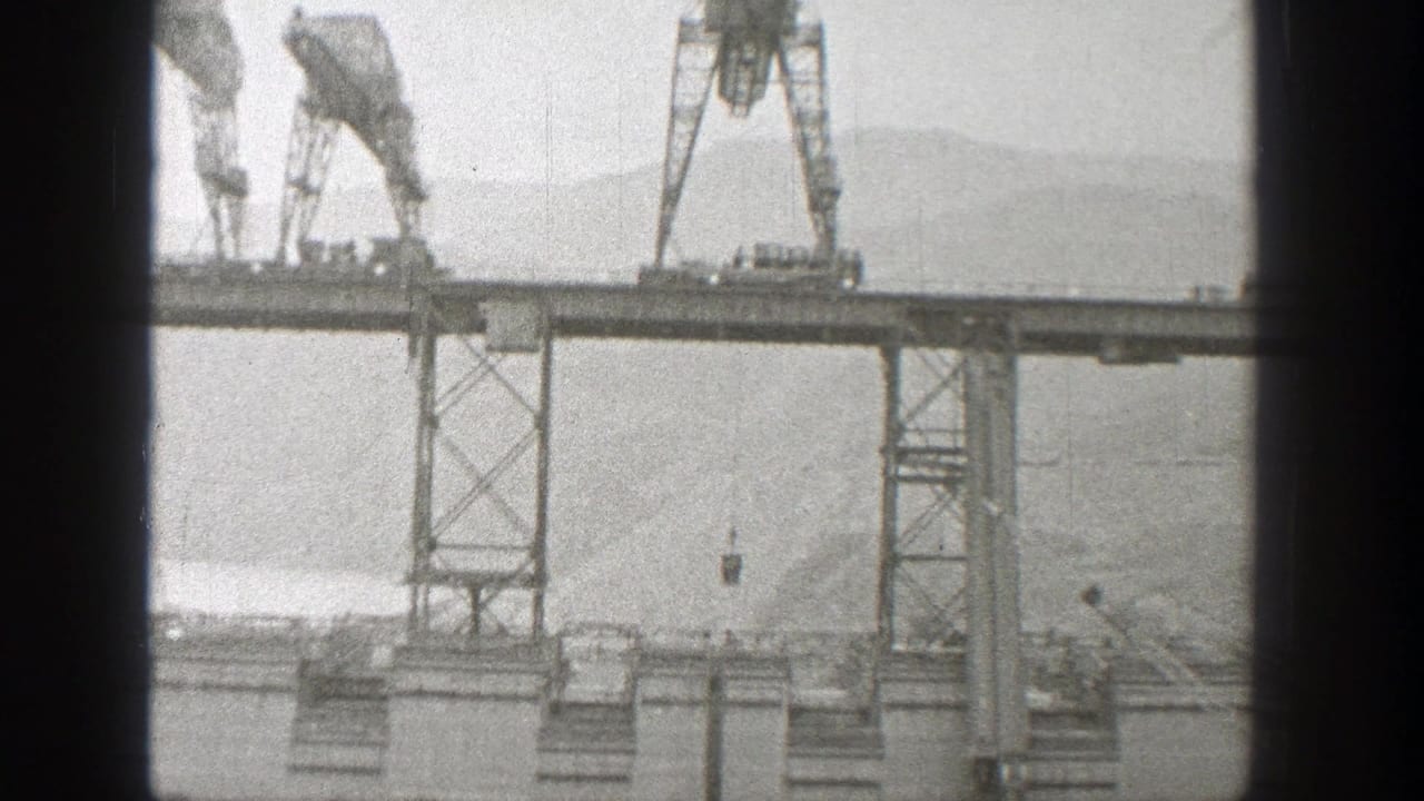 Cranes on a bridge span lowering equipment over water and hills.