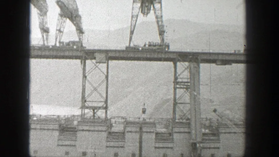 A 1938 Washington construction view shows crane machinery on the bridge span and a hanging load above waterfront supports.