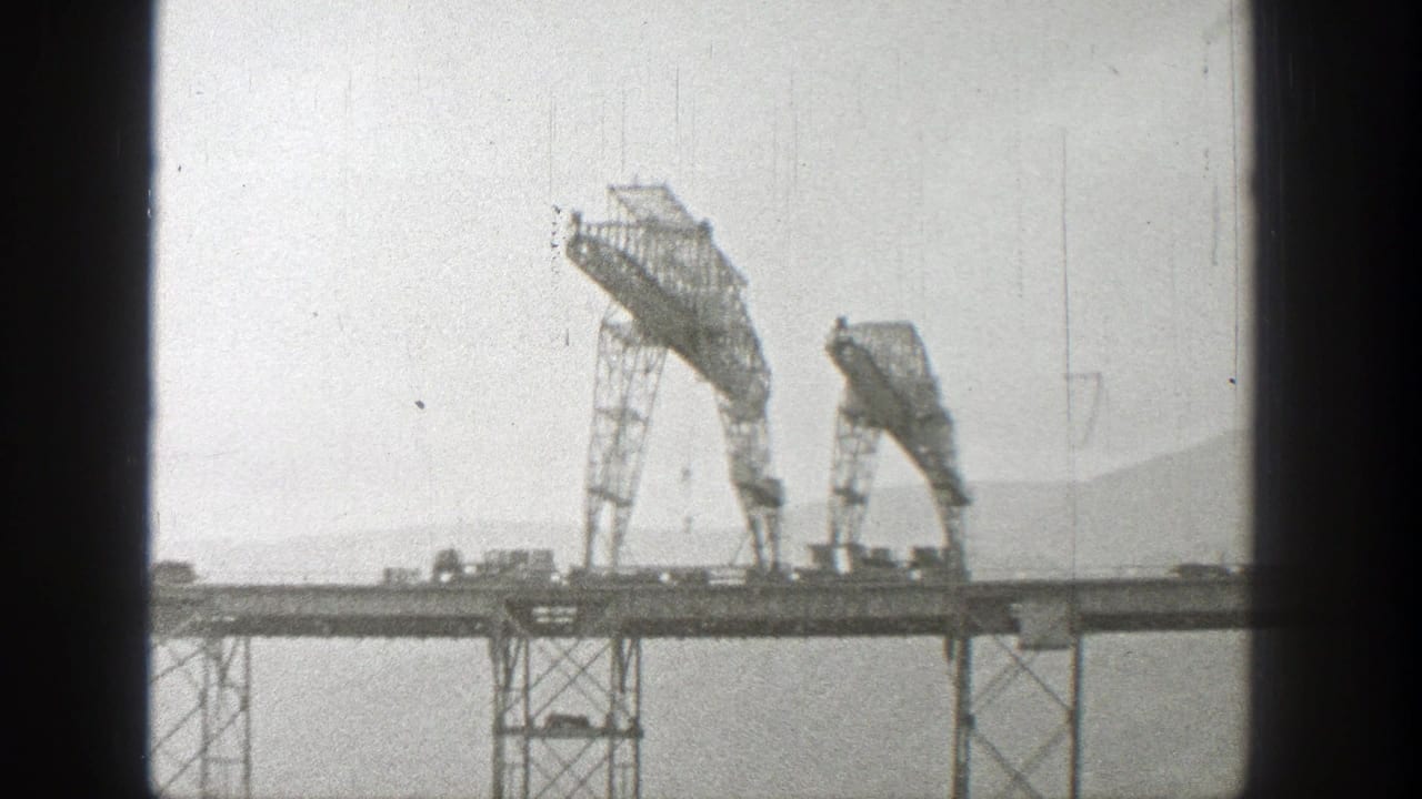 Steel bridge spans the frame with two raised metal structures and a hazy hillside beyond.
