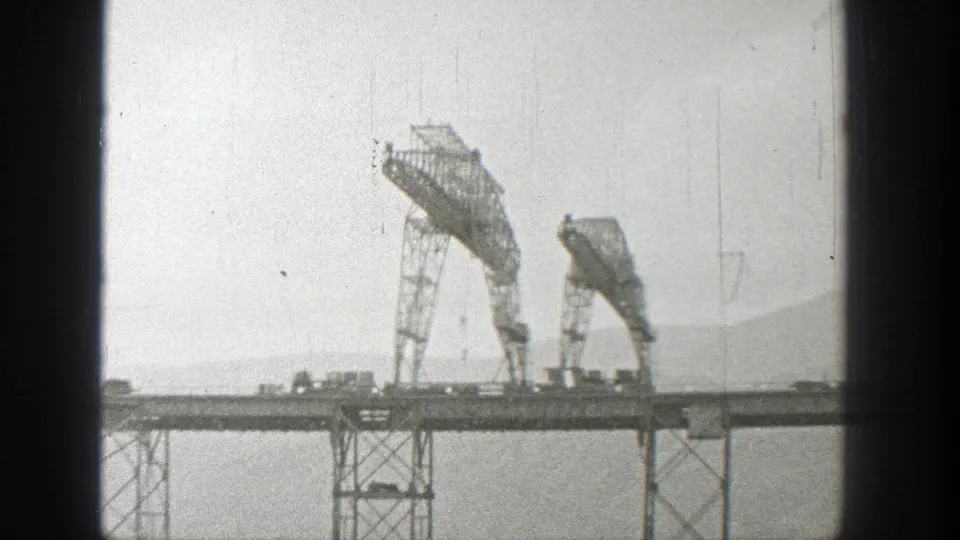 1938 Washington 8mm frame showing a steel truss bridge with two large raised metal sections, sparse roadway traffic, haze, and distant hillside.