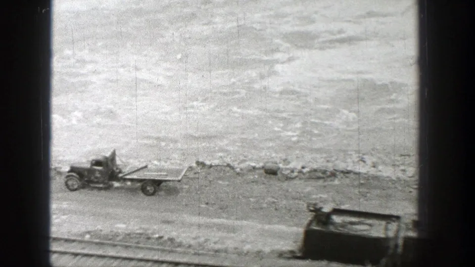 1938 Washington 8mm frame showing a flatbed truck or trailer and abandoned car body near tracks beside a turbulent riverbank.
