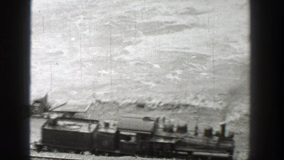 Steam locomotive moves through a Washington rail scene in 1938, passing a parked vehicle near the riverbank.