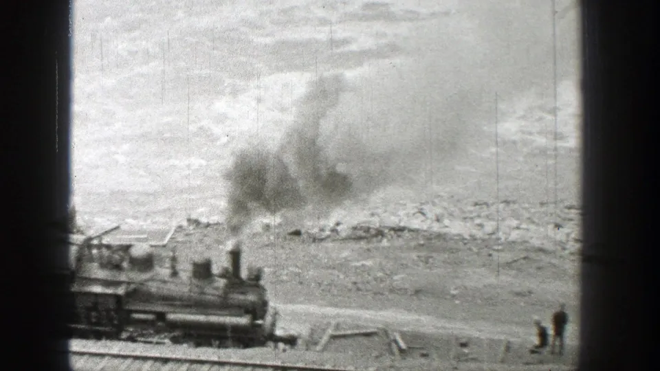 1938 Washington frame with a steam locomotive, smoke plume, riverbank, and two distant figures standing near the tracks.