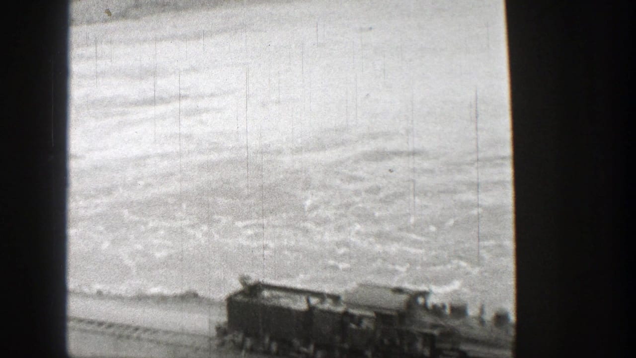 Washington 1938 home-movie frame showing a steam train along a riverside track, with turbulent water behind it.