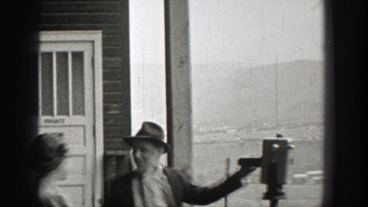In 1938 Washington home-movie footage, a suited man in a fedora stands by a coin-operated viewing scope as a woman passes nearby.