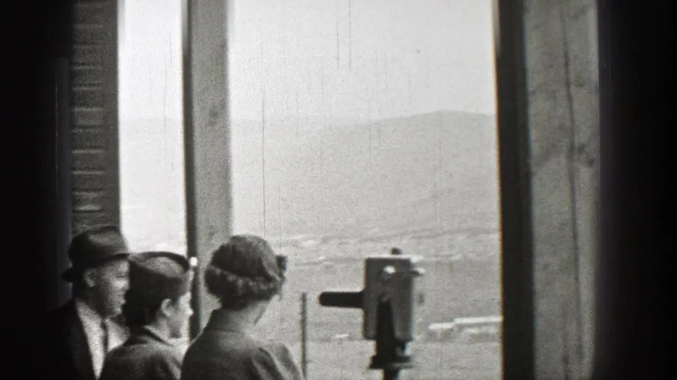 Adults in 1930s clothing gather near an overlook viewer in Washington, with distant hills visible through the open side of the structure.