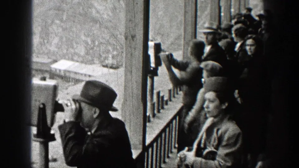 At a Washington overlook, a man uses a public binocular viewer while a woman in period dress stands beside the railing.