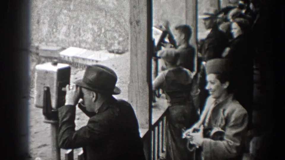 A man peers into a coin-operated viewer as a woman with a small camera or case stands beside him in 1938 Washington footage.