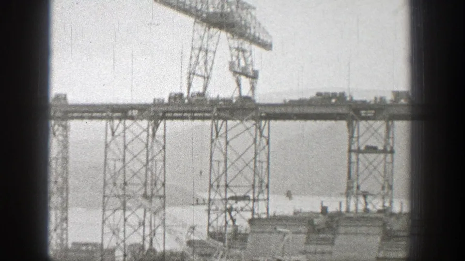 1938 Washington 8mm frame showing steel bridge framework and a gantry crane above water, seen from a distant home-movie viewpoint.