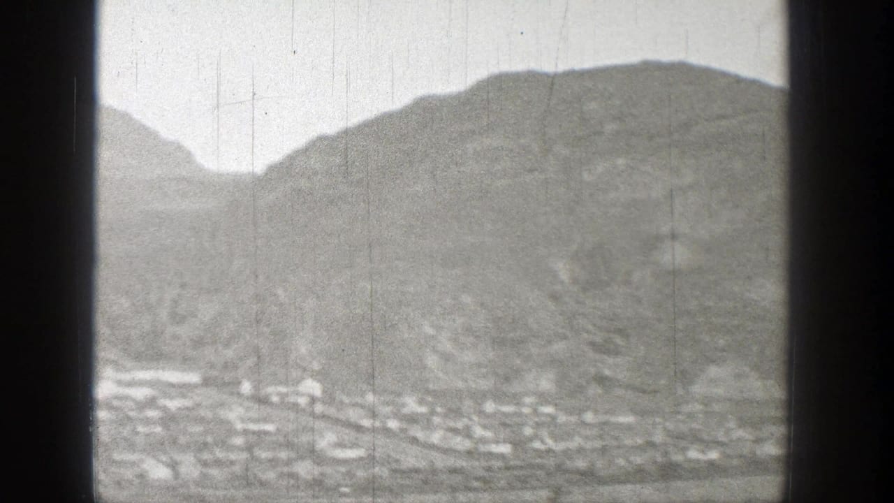 1938 Washington 8mm frame showing a small distant settlement at the base of rugged hills under a pale cloudy sky.
