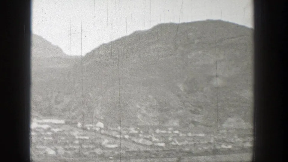 1938 Washington 8mm frame showing a small distant settlement at the base of rugged hills under a pale cloudy sky.