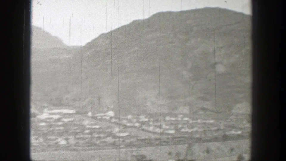 Black-and-white 8mm view of a small Washington settlement beneath a broad barren hill, softened by haze and film wear.