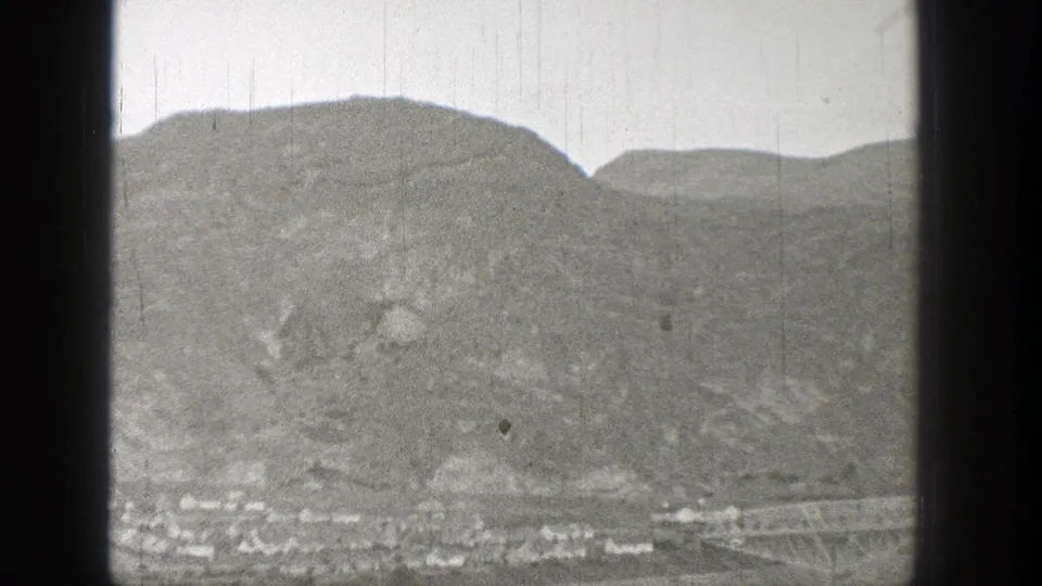 1938 Washington home-movie frame showing a far-off settlement beneath rocky hills, with a possible bridge at the lower right.