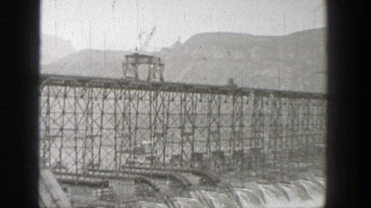 1938 Washington 8mm frame of a truck moving across an elevated steel bridge over water, with hills in the background.