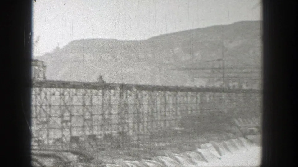 1938 Washington frame showing trucks on an elevated steel span, with trestle supports, water, and hills beyond.