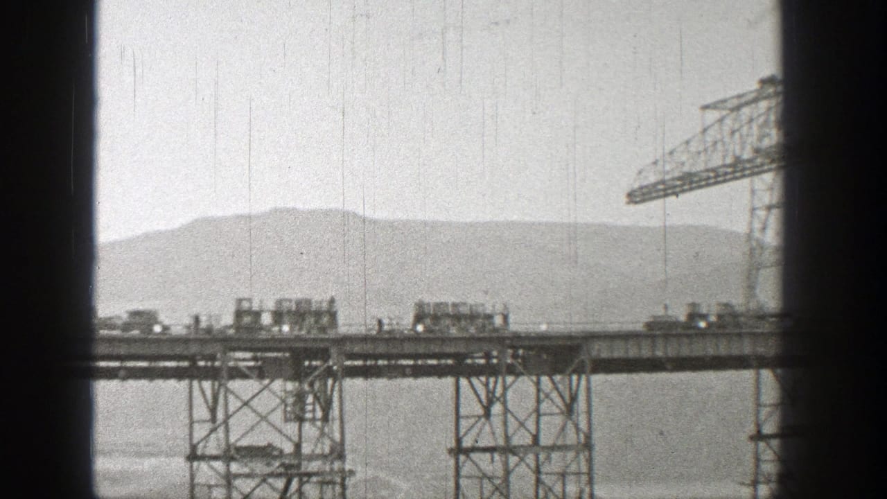 Train cars crossing a high steel bridge with mountains in the background.