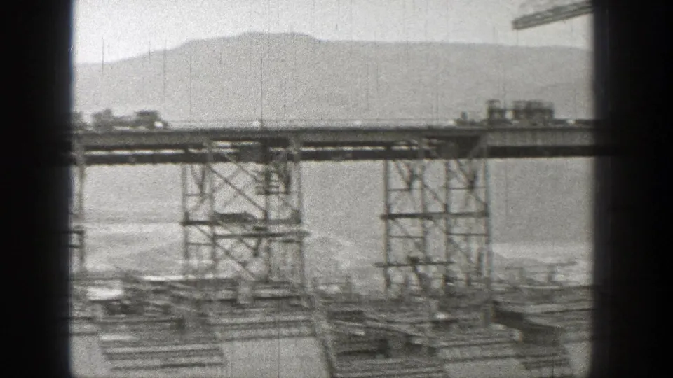 1938 Washington home-movie frame showing a slightly blurred train crossing a high steel bridge over water or open ground.