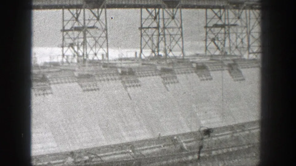 Black-and-white 8mm frame of dam construction in Washington, with steel towers, concrete surfaces, and small work details visible.