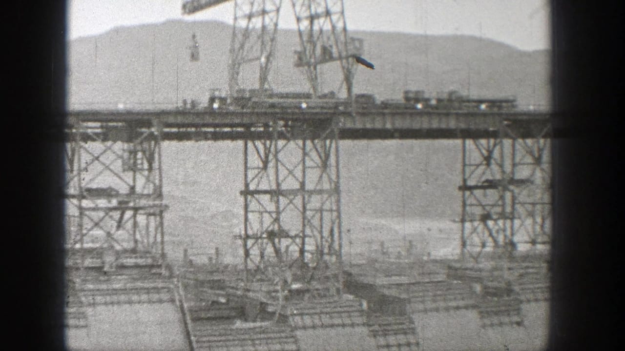 Steel construction towers and a partial span over flowing water with hills behind.
