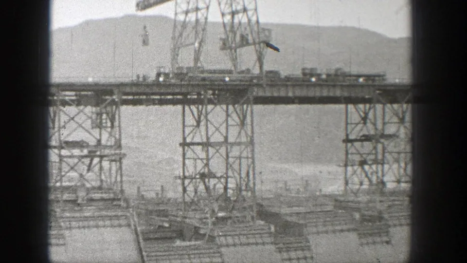 1938 Washington 8mm frame showing steel support towers and a partially built bridge or dam structure above moving water.
