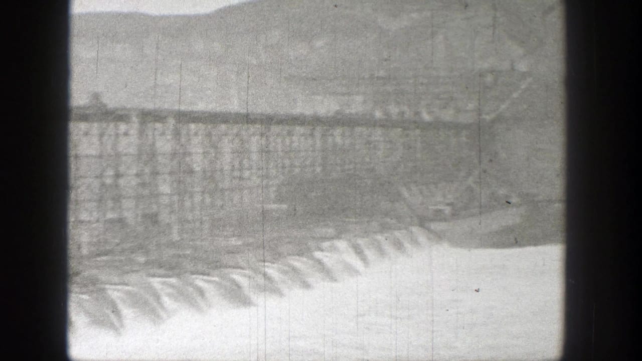 Water spills over a concrete dam with a steel structure above it.