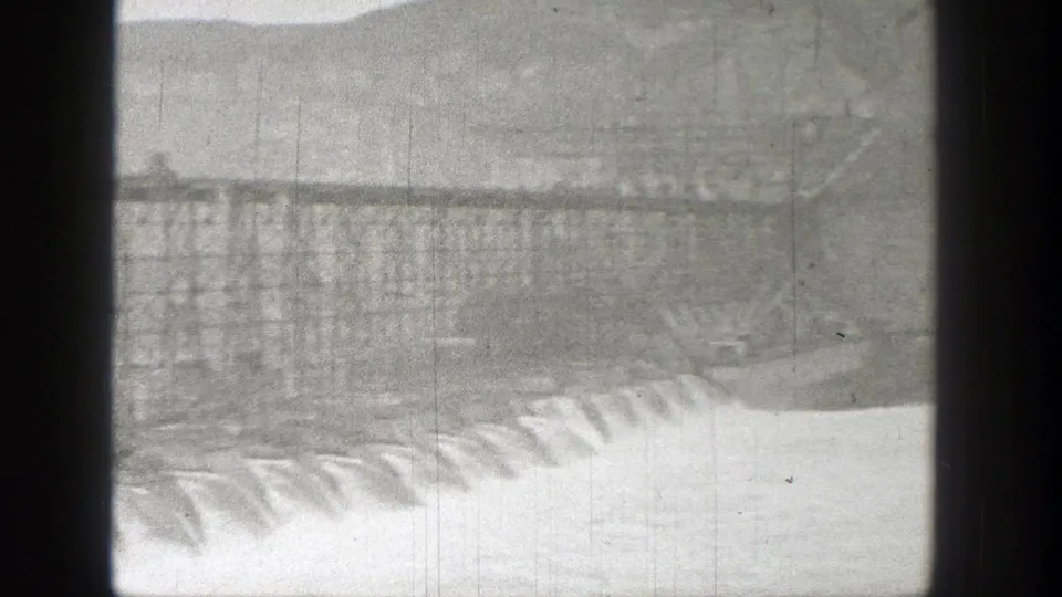1938 Washington home-movie frame showing water cascading over a concrete dam beneath a steel roadway or bridge structure.