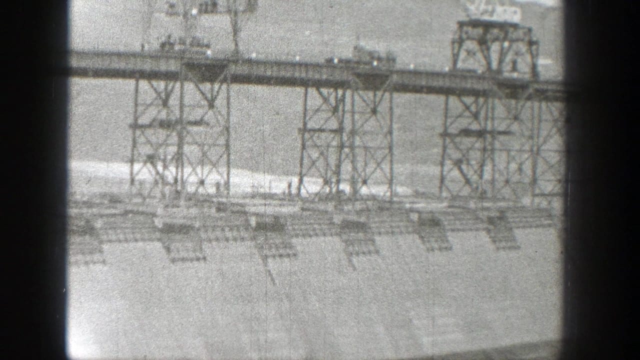 1938 Washington 8mm frame showing a distant industrial metal framework above a sparse graded landscape.