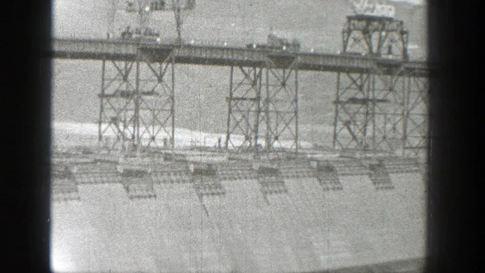 1938 Washington 8mm frame showing a distant industrial metal framework above a sparse graded landscape.