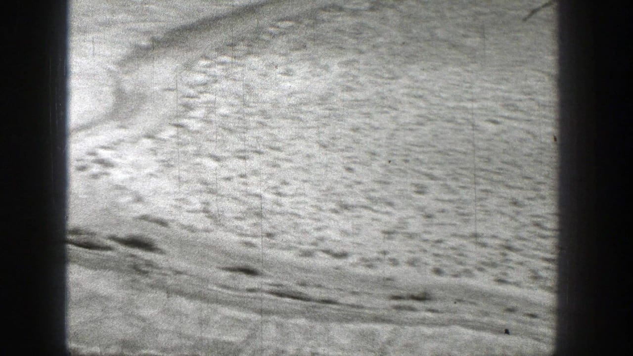1938 Washington 8mm frame showing textured dry riverbed ground with scattered marks and dark vertical frame-edge obstructions.