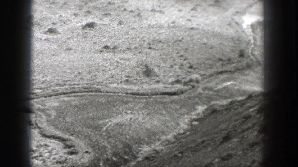1938 Washington home-movie frame showing cracked or tracked dry riverbed surface with stones and heavy edge shadows.