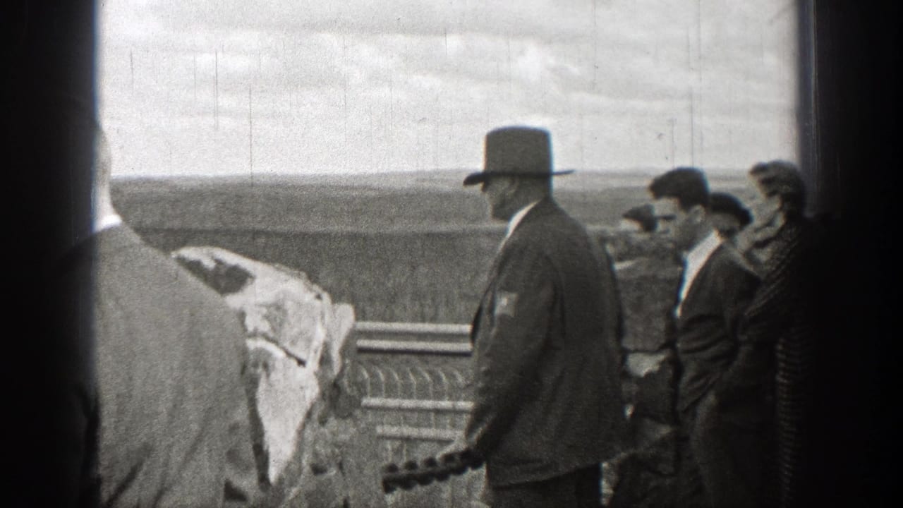 Men in suits and hats stand by a stone railing at an outdoor overlook.