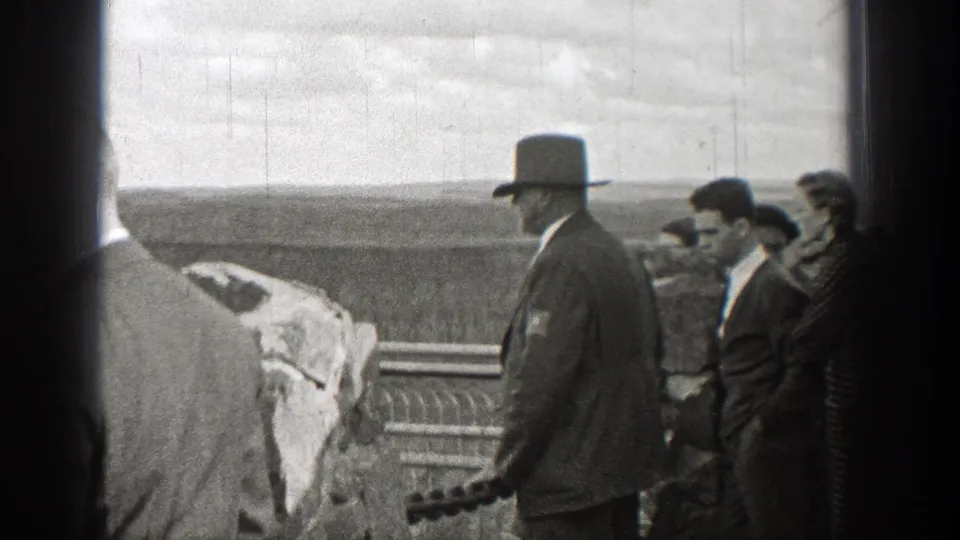 In 1938 Washington home-movie footage, men in suits and hats gather beside a stone railing while one holds a camera near a broad landscape.