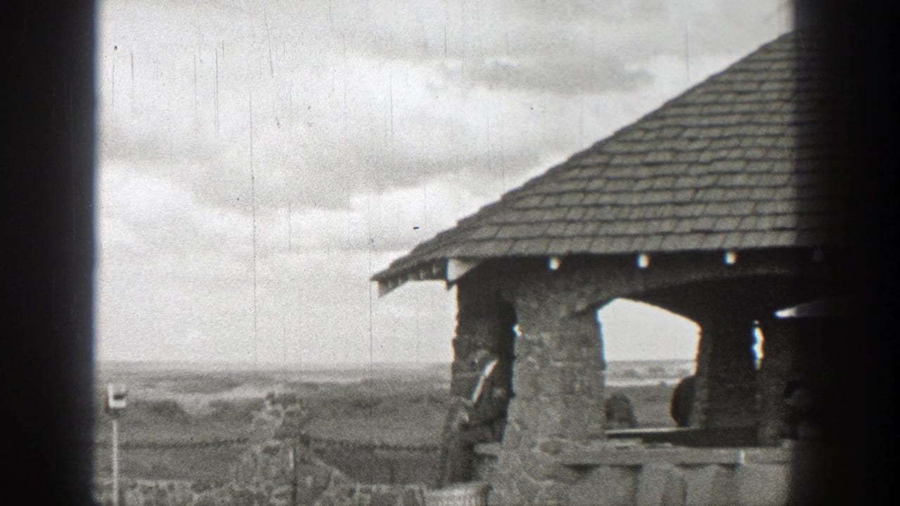 Stone pavilion roof and railing overlook a broad cloudy landscape.