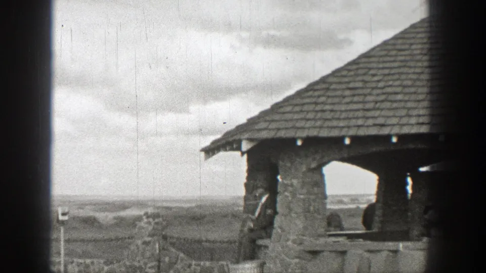 A rustic stone pavilion with a shingled roof frames a cloudy Washington landscape in 1938 archival home-movie footage.