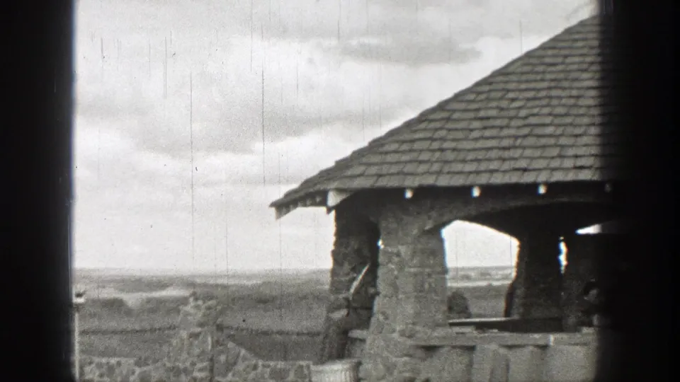 A repeated 1938 Washington home-movie view holds on the stone pavilion and railing, with a cloudy sky and low landscape beyond.