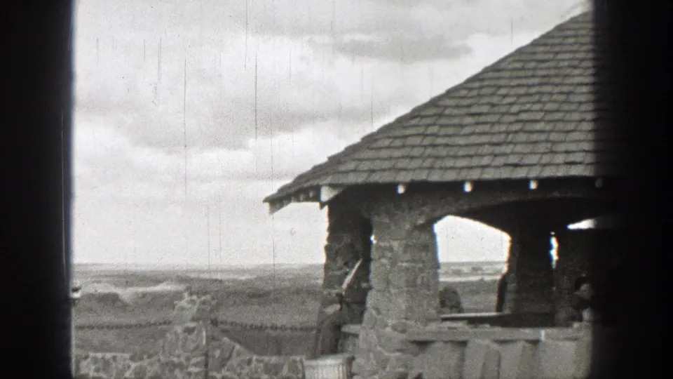 1938 Washington 8mm frame showing a rustic stone shelter with a shingled roof beside an open overlook.