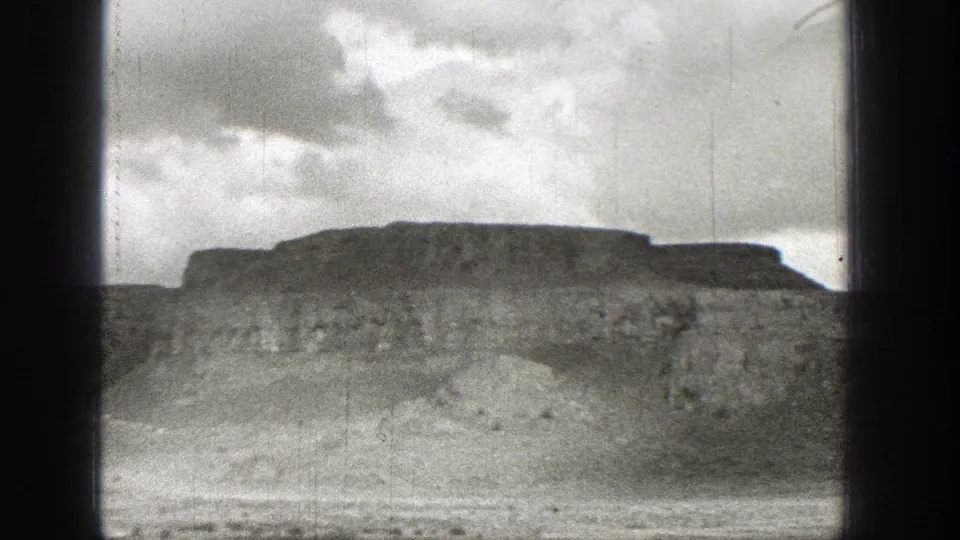 1938 Washington 8mm frame of a mesa-like ridge or bluff seen across dry open terrain under a clouded sky.