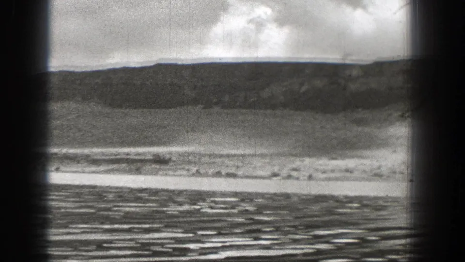 1938 Washington 8mm frame showing rippled water, a pale shore, and a broad ridge beneath clouds.
