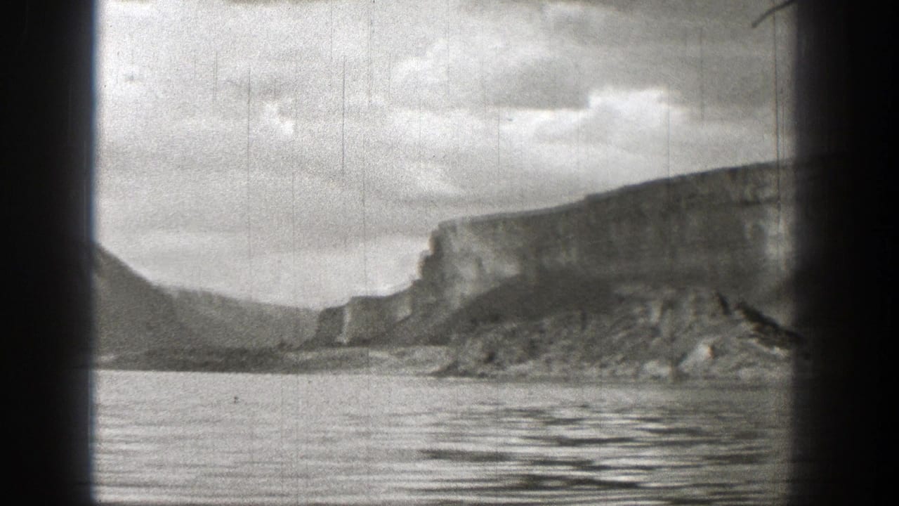 Black-and-white 1938 Washington home-movie frame showing open water, a distant rocky cliff, low mountains, and cloudy sky.