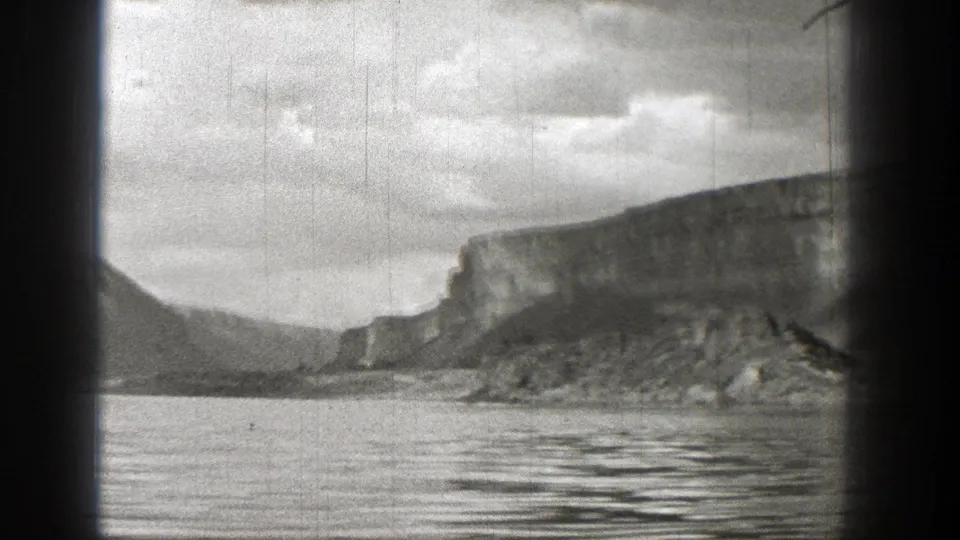 Black-and-white 1938 Washington home-movie frame showing open water, a distant rocky cliff, low mountains, and cloudy sky.
