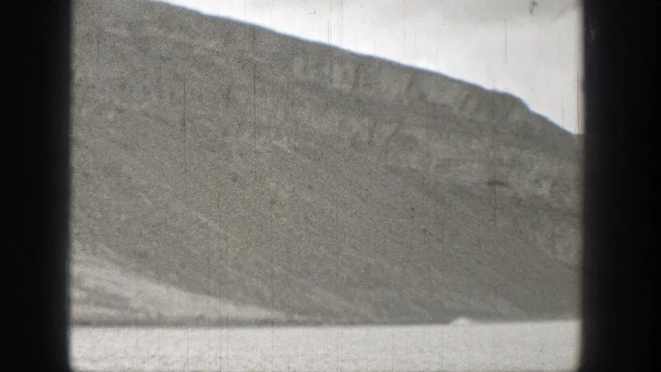 1938 Washington home-movie frame showing a broad sloping mountainside beside open water, with grain and scratches visible.