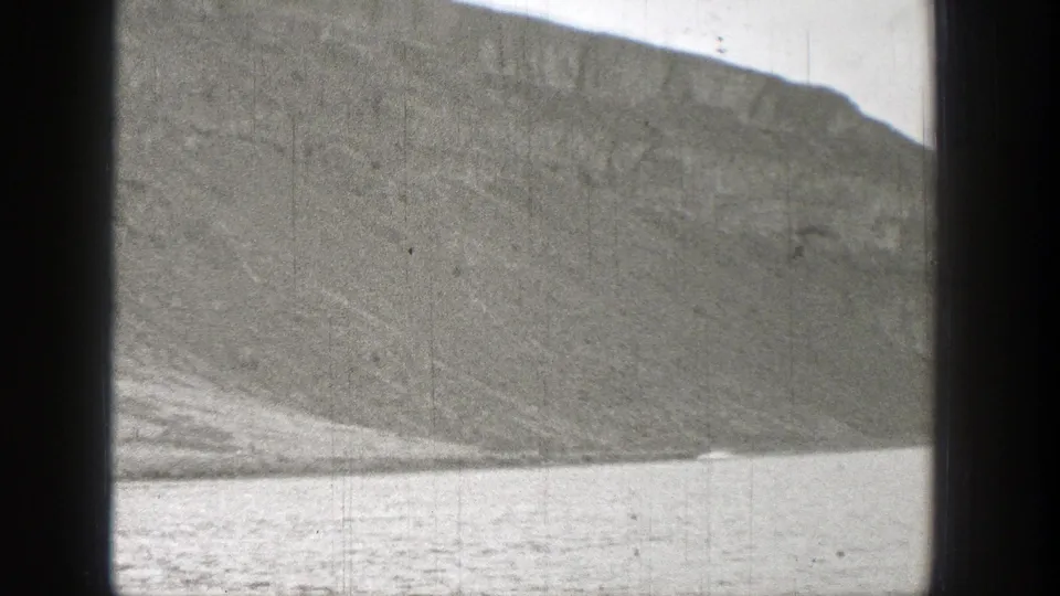 Black-and-white 8mm frame from Washington showing a rocky shoreline slope meeting open water, with cloudy sky mostly out of view.