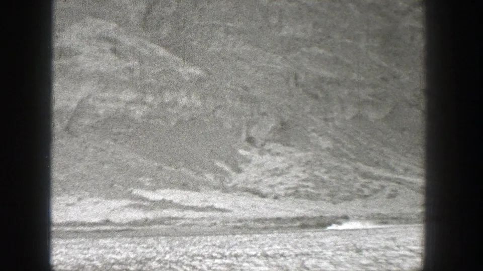 1938 Washington 8mm frame with a small bright craft or aircraft moving near the right side of the frame, smoke trailing across an open strip.