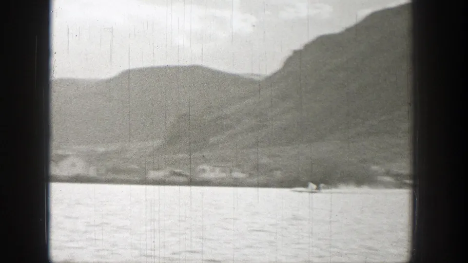 1938 Washington 8mm frame showing a small speedboat on calm water below distant hills, viewed through dark vertical framing.