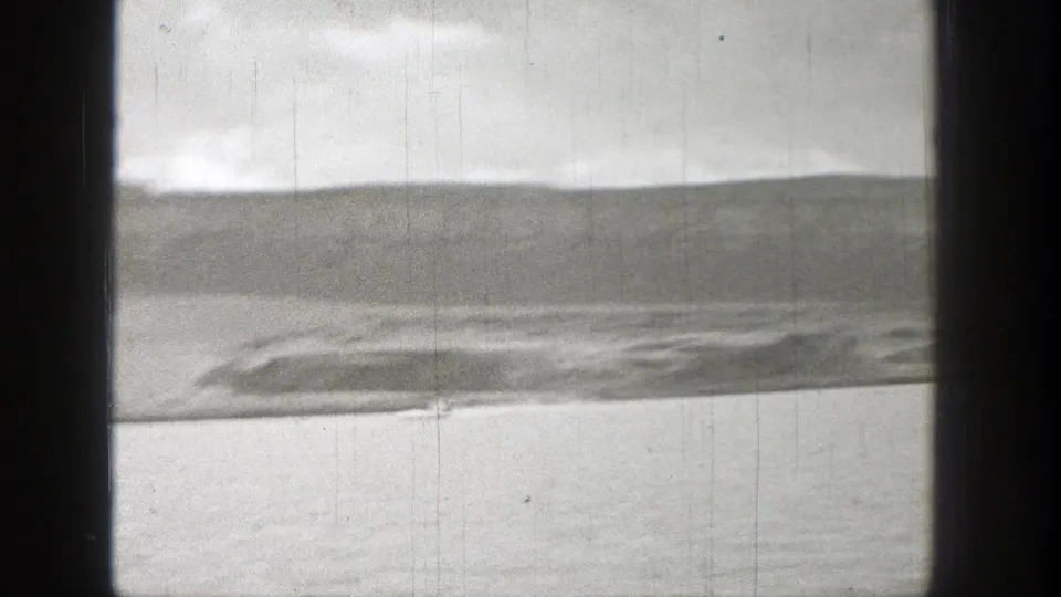 A 1938 Washington shoreline view on 8mm film, with calm water, distant hills, and dark window-like framing in the foreground.