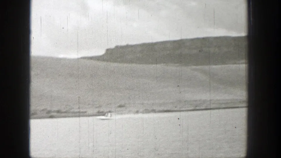 1938 Washington 8mm view of a small speedboat and pale wake on calm water, with a distant headland and dark foreground framing.