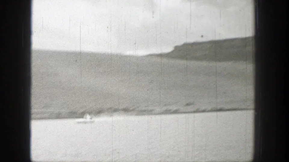 1938 Washington 8mm frame showing a small boat crossing a lake below distant hills, with heavy gate shadows and film wear.