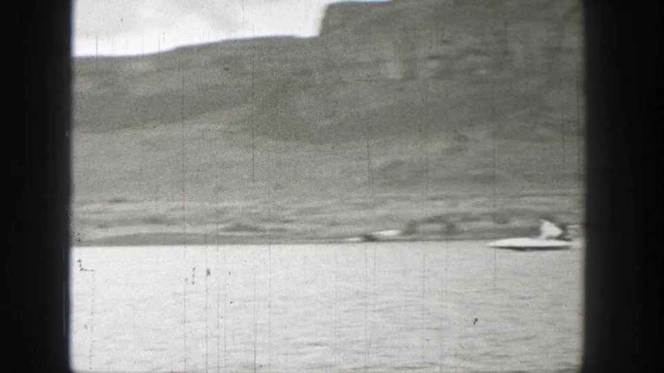 1938 Washington lake view with a small boat near the right edge, low hills beyond the water, and visible 8mm scratches.