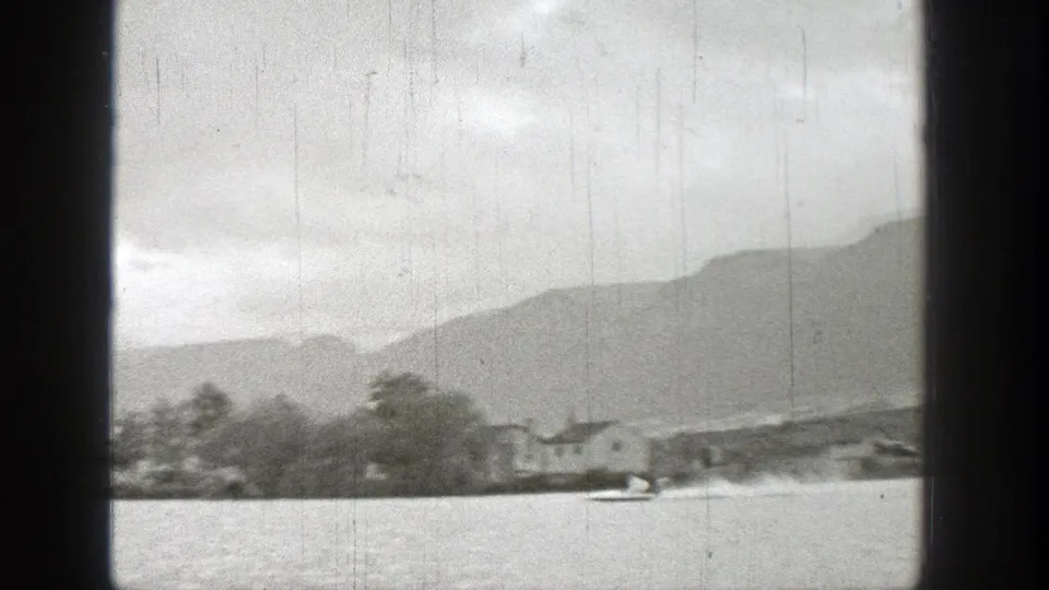 1938 Washington lake scene showing low mountains, shoreline trees, and a small boat near the right edge of the frame.